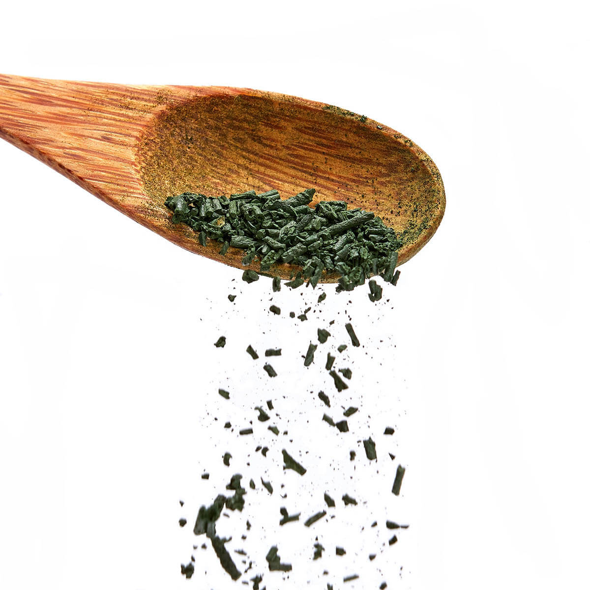 Bio Spirulina Granulat von Algenmarkt rieselt von einem Holzlöffel vor weißem Hintergrund