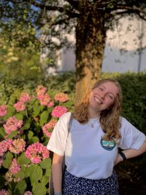 Lächelnde junge Frau im Algenmarkt-Shirt vor blühenden Hortensien